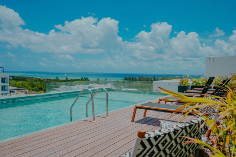 Rooftop con alberca infinity y vista panorámica al mar Caribe, con camastros y diseño moderno, dentro de un desarrollo residencial de lujo con departamentos en venta en Playa del Carmen, ideal para disfrutar el equilibrio entre exclusividad y confort.