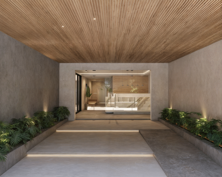 Entrada principal del desarrollo Macondo Punta Esmeralda con iluminación cálida, techo de madera, paredes de concreto pulido y jardineras laterales con plantas tropicales, dentro de los departamentos en venta en Playa del Carmen.