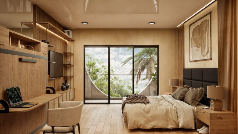 Interior de una unidad en Macondo Corazón con terraza, cama con cabecera tapizada, escritorio de trabajo con silla beige, mobiliario de madera natural, arte en tonos neutros y ventanal con vista a palmeras y cielo azul. Espacio moderno y luminoso dentro de los departamentos en venta en Playa del Carmen.